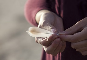Zwei Hände einer Person halten eine weiße Vogelfeder behutsam.