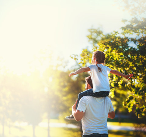 Auf den Schultern eines Mannes sitzt ein Kind, welches die Arme in die Luft streckt. 