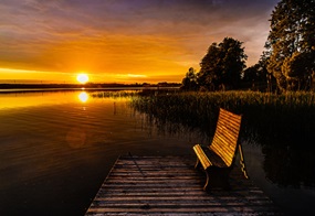 Panoramaaufnahme von einem Sonnenuntergang vor einem See mit einer Bank