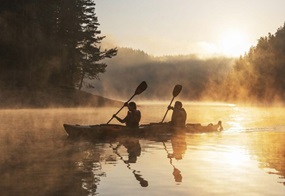 Zwei Personen paddeln im Sonnenaufgang mit einem Kanu über eine See