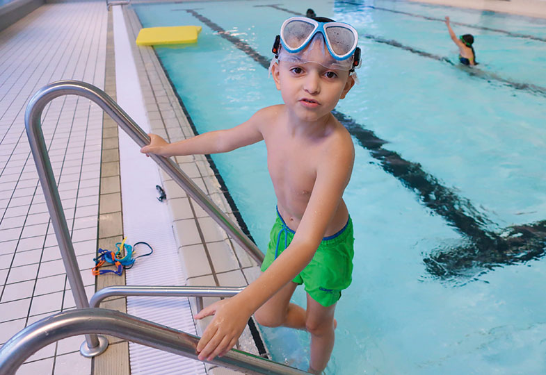 Ein Kind mit einer Taucherbrille auf dem Kopf steigt an der Leiter ins Schwimmbecken.
