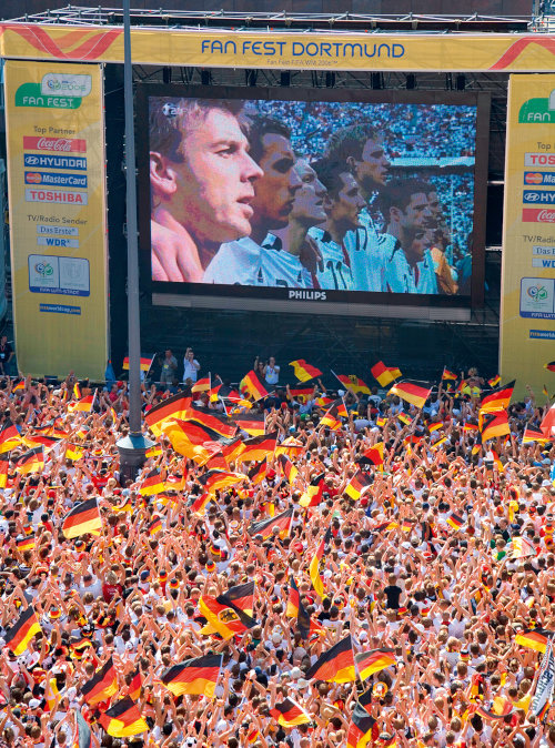 Viele Menschen mit wehenden Flaggen schauen auf eine große Leinwand