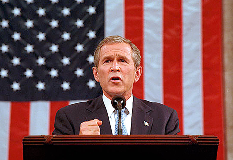 George W. Bush hält eine Rede. Im Hintergrund die Flagge der USA