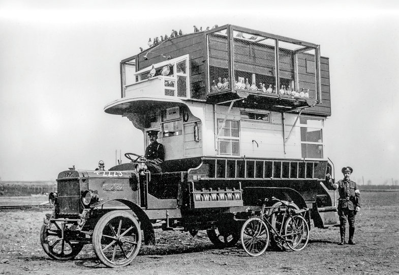Schwarz-Weiß Foto eines alten Autos mit riesigem Taubenkäfig auf der Ladefläche