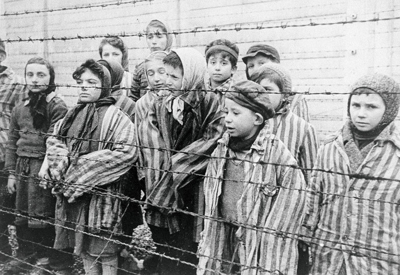 Mehrere Kinder stehen hinter einem Stacheldrahtzaun und schauen traurig