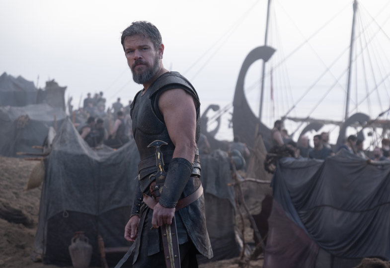 Matt Damon als Odysseus blickt in die Kamera, im Hintergrund sind Schiffe