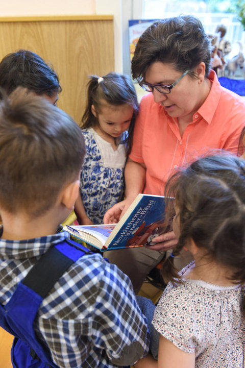 Kinder stehen um eine Erzieherin, die aus einer Kinderbibel vorliest.