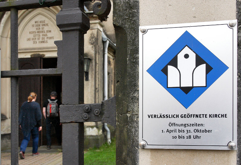 Ein Hinweisschild mit der Aufschrift "Verlässlich geöffnete Kirche" und deren Öffnungzeiten