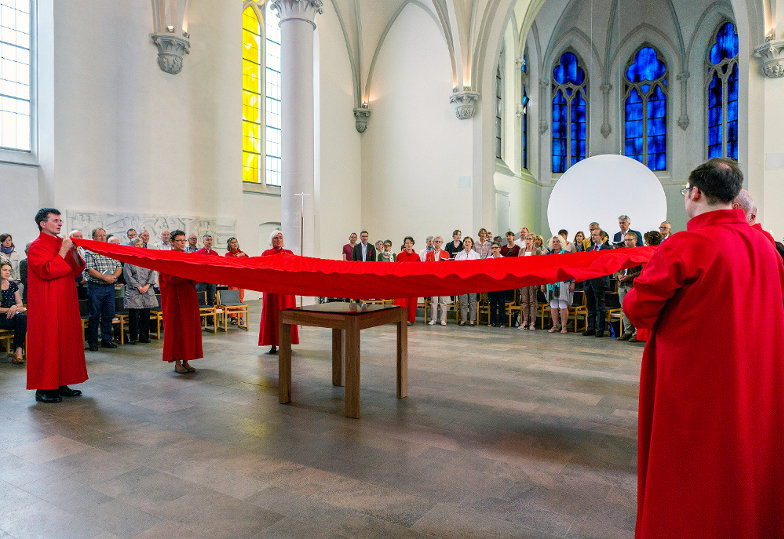 Im Pfingstgottesdienst spannen liturgische Dienste ein rotes Tuch über dem Altar