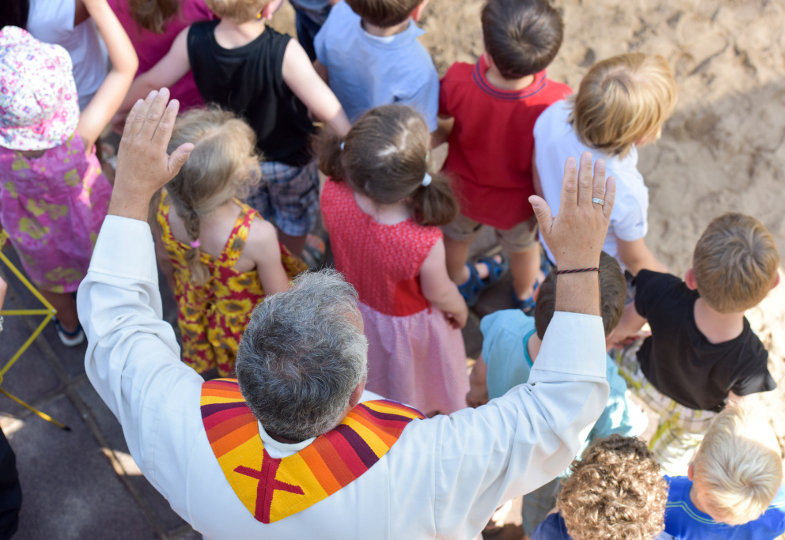 Zum Segen breitet ein Priester seine Hände über Kindergartenkinder aus