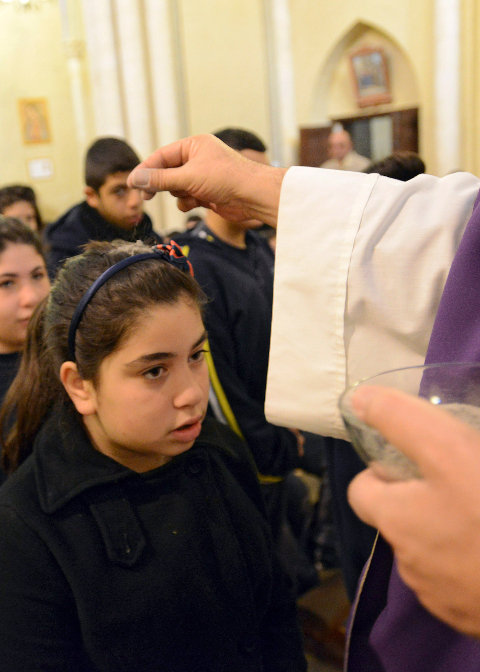 Am Aschermittwoch streut ein Priester einem Mädchen Asche auf den Kopf