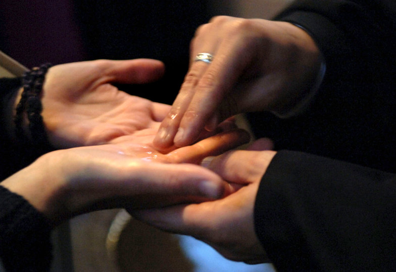 Bei einem Tauferinnerungsgottesdienst zeichnen zwei Teilnehmer einander mit Weihwasser ein Kreuz in die Hand