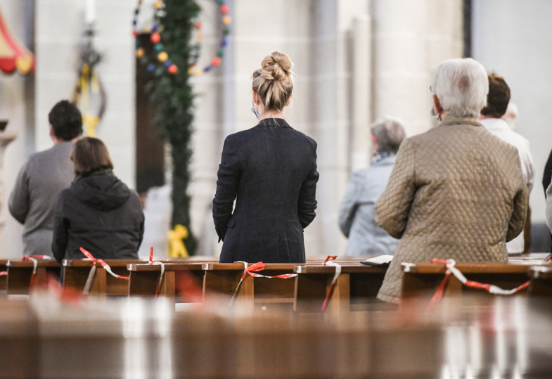 Gottesdienstfeiernde mit Mundschutz in Kirchenbänken mit Absperrband