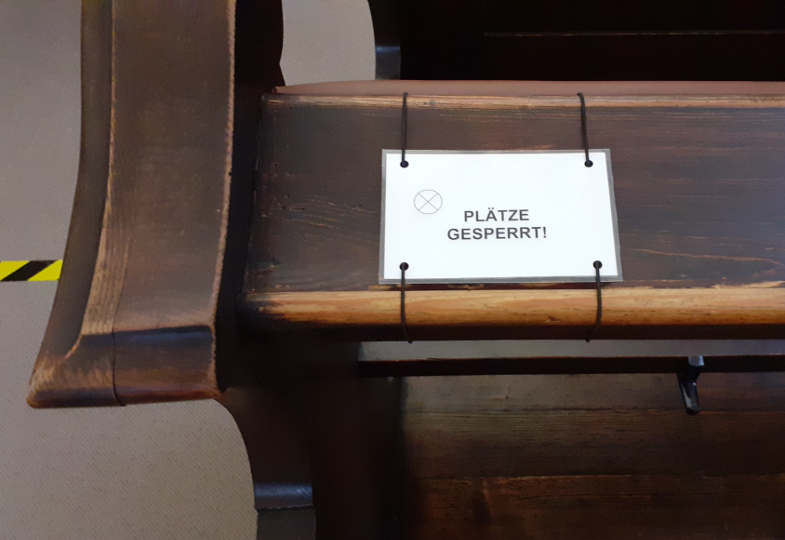Ein mit Schnur an einer Kirchenbank befestigtes Hinweisschild