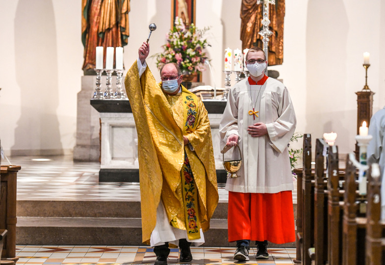 Ein Priester sprengt beim Taufgedächtnis Weihwasser über Gläubige.