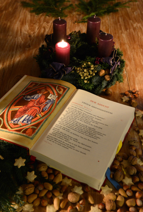 Ein aufgeschlagenes Evangeliar vor einem Adventskranz mit brennender erster Kerze 