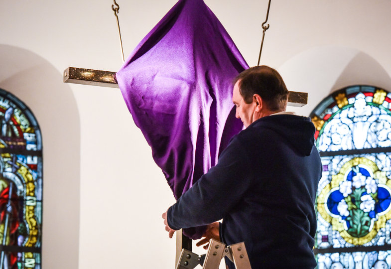 Ein Sakristan verhüllt ein Kruzifix mit einem violetten Tuch