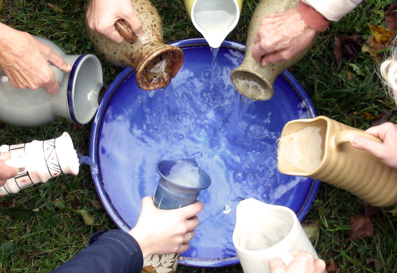 Verschiedene Menschen gießen Wasser aus unterschiedlichen Krügen in eine große Schale, die überläuft