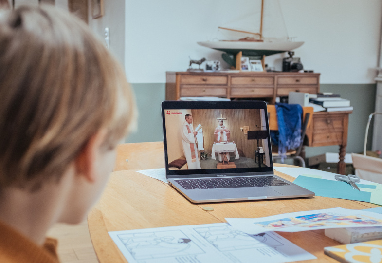 Ein Kind schaut am Laptop eine gestreamte Eucharistiefeier.