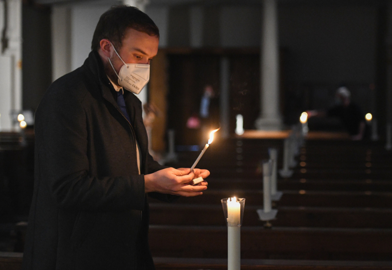 In einer dunklen Kirchen werden Kerzen entzündet.