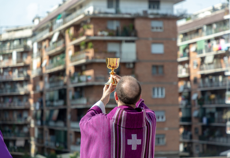 Mit Blick auf Hochhäuserfassaden erhebt ein Priester den Kelch