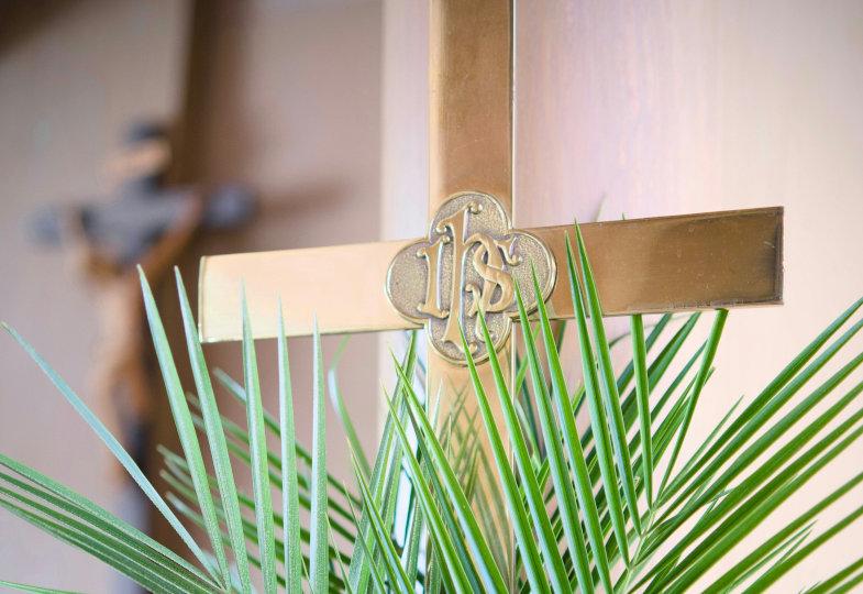 Ein Palmzweig lehnt vor einem Kreuz