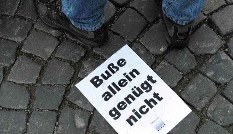 Plakat mit Aufschrift "Buße allein genügt nicht" liegt auf dem Boden