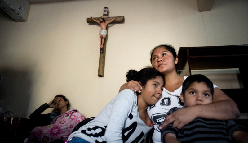 Geflüchtete Mutter umarmt ihre Kinder unter einem Kreuz