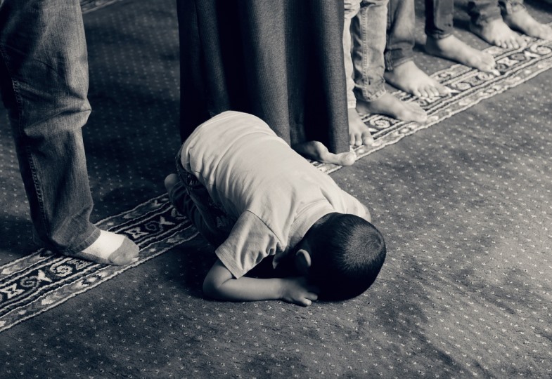 Ein muslimischer Junge betet auf einem Gebetsteppich.