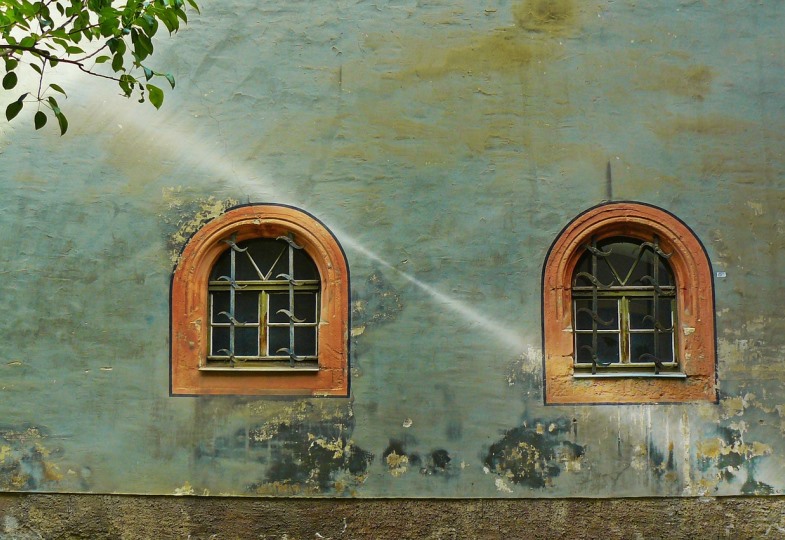 Eine Hausfassade mit zwei Fenstern wird von einem Sonnenstrahl getroffen.