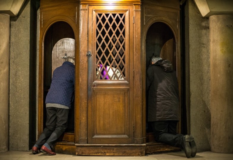 Menschen beichten bei einem Priester im Beichtstuhl.