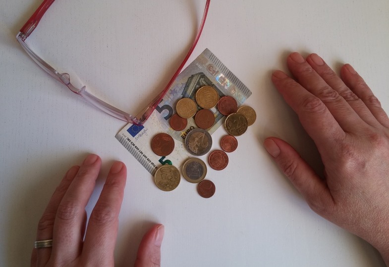 Hände, die eine kleine Summe Geld in Münzen und Scheinen abzählen.