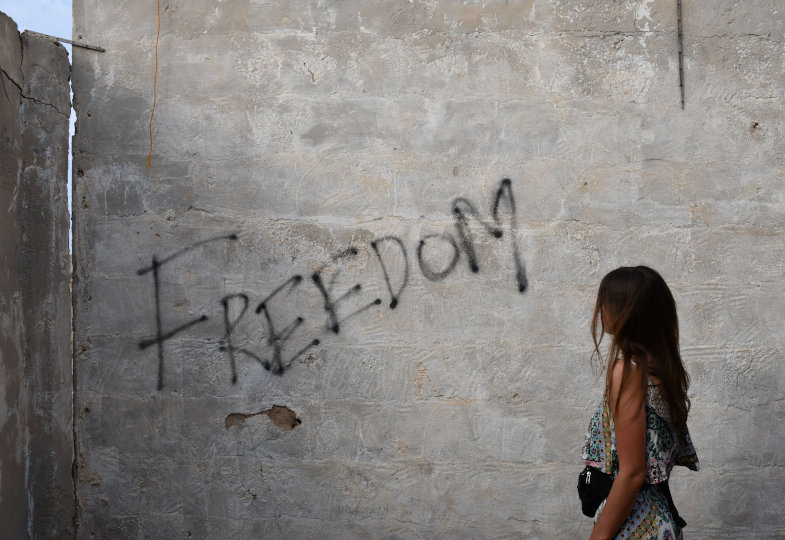 Eine Frau steht vor einer Mauer mit dem Schriftzug Freedom