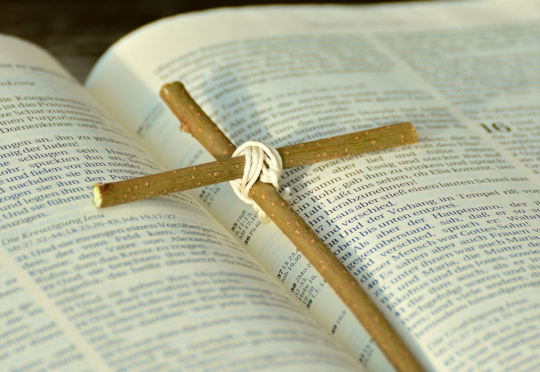 Ein kleines Kreuz liegt auf einer aufgeschlagenen Bibel