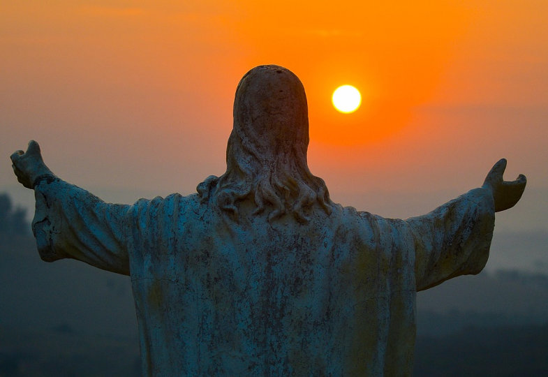 Christussstatue von hinten mit Blick auf die untergehende Sonne