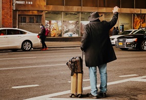 Ein Mann steht mit einem Koffer in der Hand an der Straße