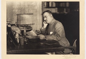  Thomas Mann, Brustbild, Halbprofil nach links, mit Brille, Kopf auf die rechte Hand gestützt, Manuskript in der linken Hand haltend.