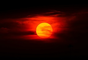Glühend orangefarbene Sonne zwischen dunklen Wolken