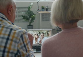 Zwei ältere Menschen telefonieren über ein Tablet mit zwei jüngeren Menschen