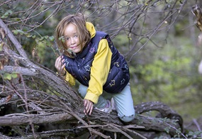 Ein Kind klettert auf einem Baum und grinst dabei.