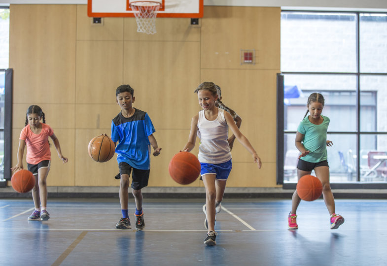 Vier Kinder spielen Basketball in einer Sporthalle.