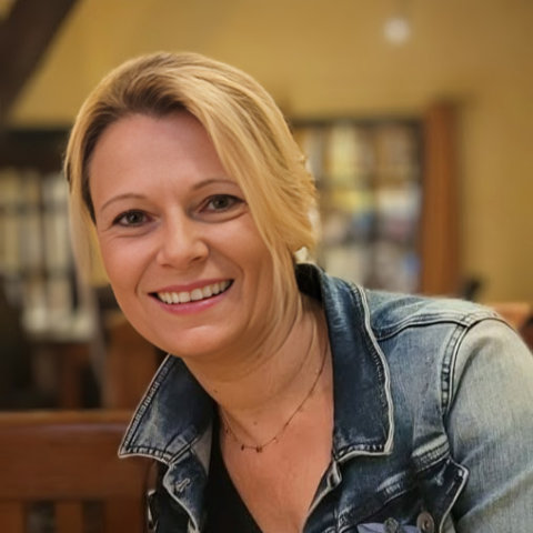 Porträt der Autorin Steffi Gijsbertsen, in Jeansjacke blonde Frau mit eine verschwommenes Bücherregal im Hintergrund 