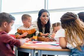 Kinder spielen freudig gemeinsam an einem Tisch mit einer Fachkraft.