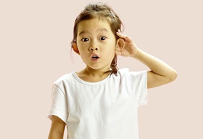 Ein Mädchen hält eine Hand hinter ihr Ohr und schaut erstaunt, als würde sie etwas Spannendes hören.