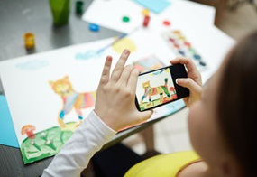 Kind fotografiert mit einem Smartphone ein selbstgemaltes Bild.