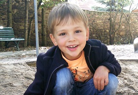 Ein lächelnder, blonder Junge hockt im Sand.