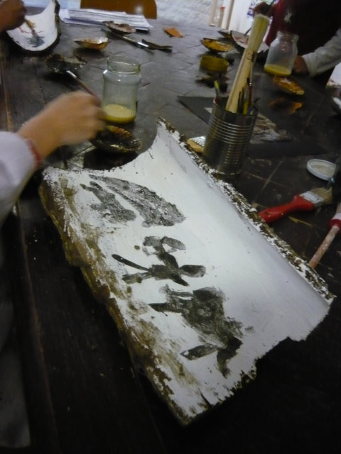 In einer Holzrinde , die weiß grundiert wurde, werden Tiere und Menschen in Schwarz hineingemalt.