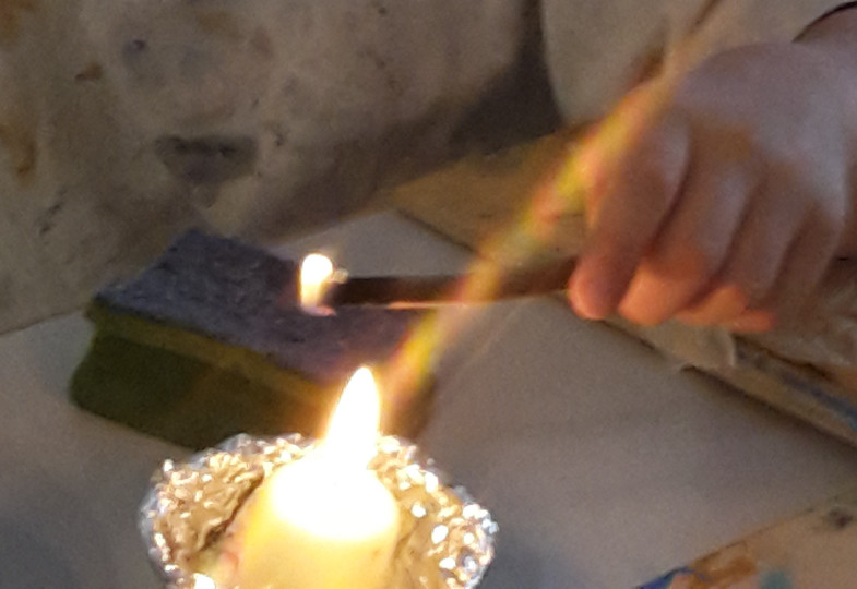 Eine Kinderhand hält einen Stock in eine Kerze.