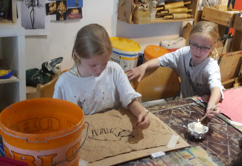 Kinder brennen eine Zeichnung in braunes Papier. Der Stift wird mithilfe einer Kerze erhitzt.