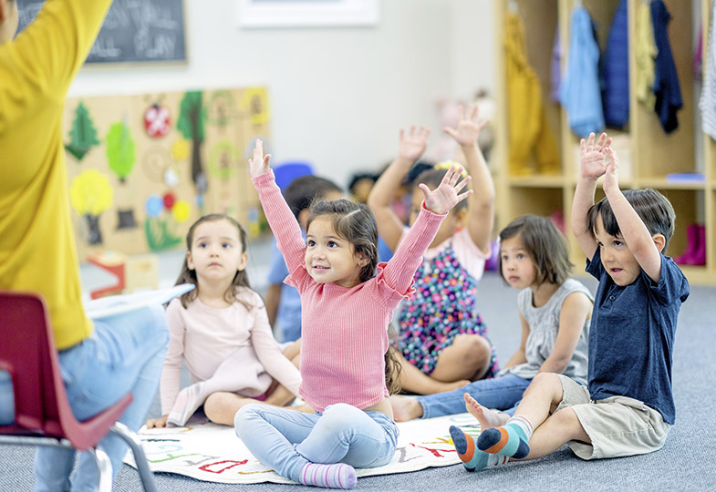 Kinder im Kindergarten sitzen auf dem Boden, einige mit erhobenen Händen.